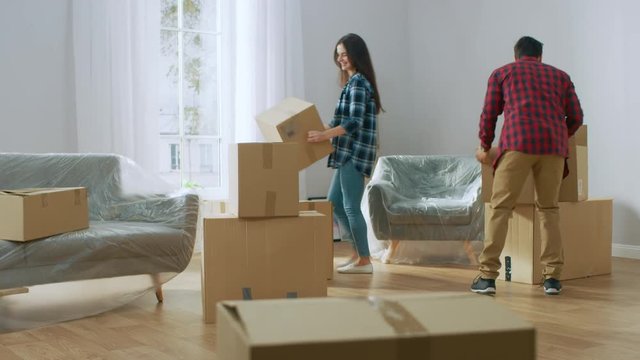 Happy Young Couple Moving Into New Apartment, Carrying Cardboard Boxes with Stuff, Having Fun, Give High Five. Young Boyfriend and Girlfriend Start Living Together, Unpacking Stuff.
