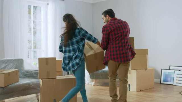 Happy Young Couple Moving Into New Apartment, Carrying Cardboard Boxes with Stuff, Having Fun, Give High Five. Young Boyfriend and Girlfriend Start Living Together, Unpacking Stuff.