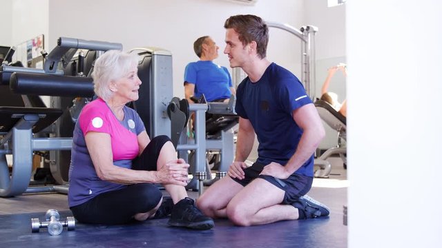 Senior Woman Discussing Exercise Program With Male Personal Trainer In Gym
