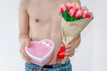 A man in swimming trunks holds flowers tulips and a heart-shaped gift box. The concept of holidays awaits women, Valentine's Day, birthday, March 8.