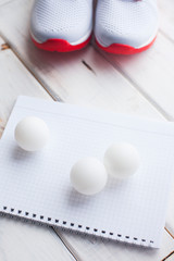 Sport fitness, weight loss concept. Ping pong racket, balls, notepad, sneakers on white wooden background