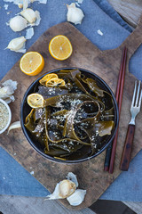 Kombu kelp soaked seaweed salad with sesame seeds, lemon, garlic in bowl on wooden board. Japanese, Chinese, Korean traditional Asian food with chopsticks. Vegan vegetarian healthy food.