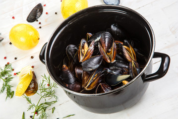 mussels in white wine sauce with glass of white wine , decorated with herbs, lemon and pepper