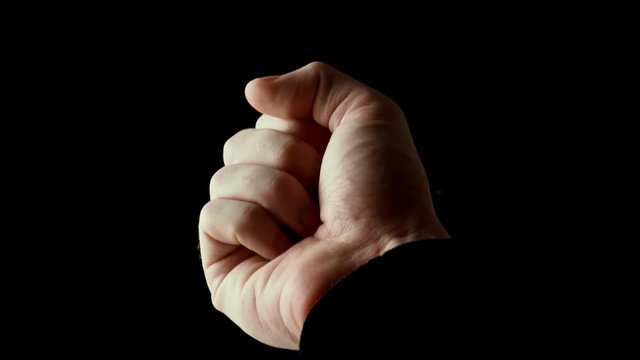 Human male palm in the rays of light isolated on black background. A man shows an open hand, then slowly clench his fingers into a fist. Stock video slow motion