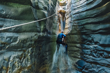 Waterfall rappelling. Man in wet suit climbs on waterfall in narrow river canyon