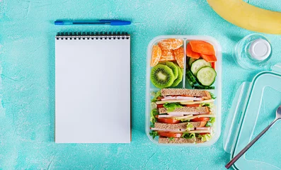 Gordijnen Schoollunchdoos met sandwich, groenten, water en fruit op tafel. Gezonde eetgewoonten concept. Plat leggen. Bovenaanzicht © timolina