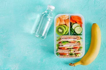 Fotobehang Schoollunchdoos met sandwich, groenten, water en fruit op tafel. Gezonde eetgewoonten concept. Plat leggen. Bovenaanzicht © timolina