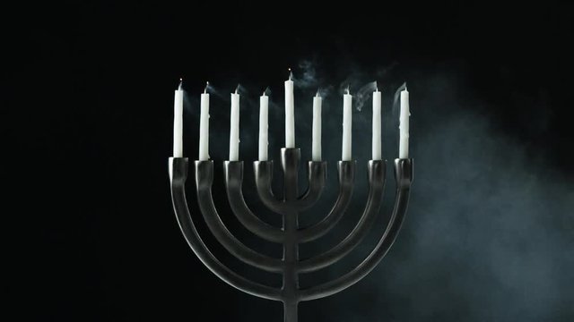 A row of nine white candles burning in a menorah are blown out, front view