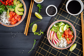 Hawaiian salmon fish poke bowl with rice, avocado, paprika, cucumber, radish, sesame seeds and...