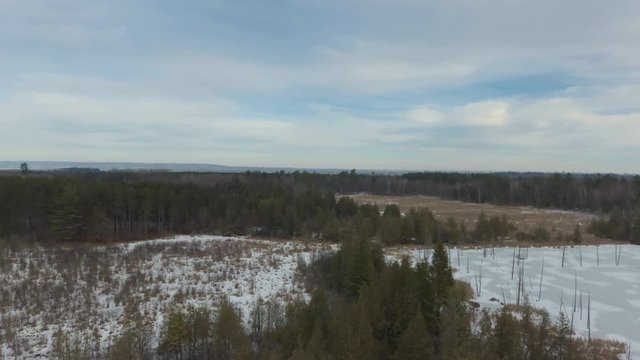 Aleria footage over a frozen pond in Canada? that wraps around some trees with a view of a city before lowering over the ice.