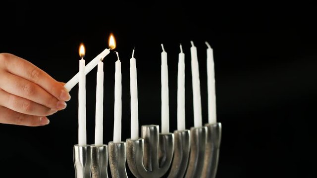 Hand lighting the nine white candles in a Jewish menorah sat on a pale marble surface, side view, close up detail
