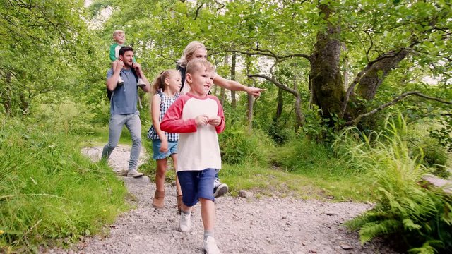 Slow Motion Shot Of Family Hiking Along Path By River In UK Lake District