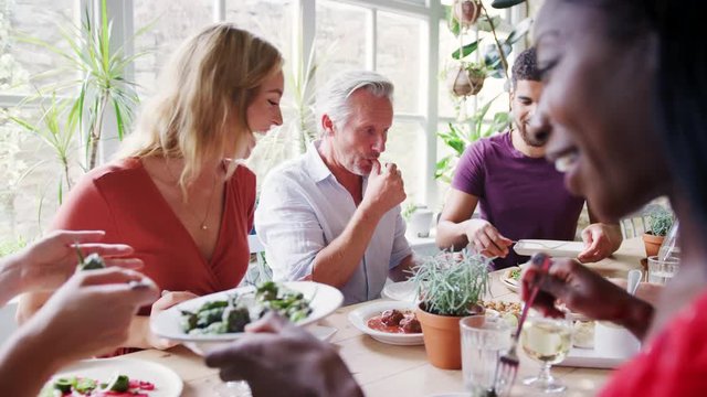 A mixed age group of adult friends eating together at a table in a small restaurant, selective focus