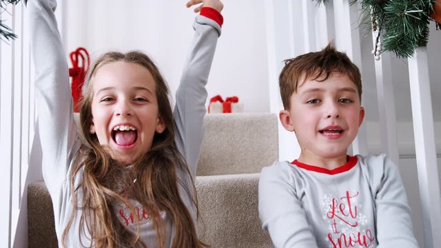 Portrait Of Two Excited Children Wearing Pajamas Sitting On Stairs Holding Stockings On Christmas Morning