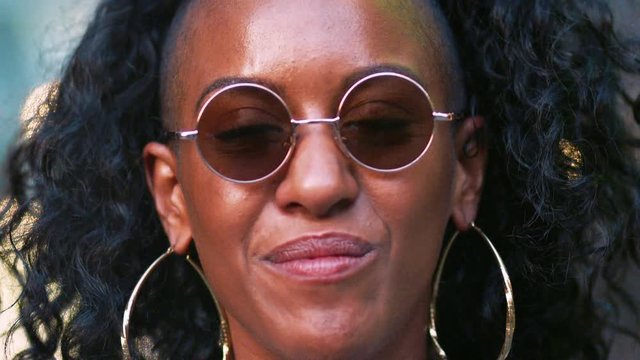 Young black woman wearing round sunglasses laughing, head shot