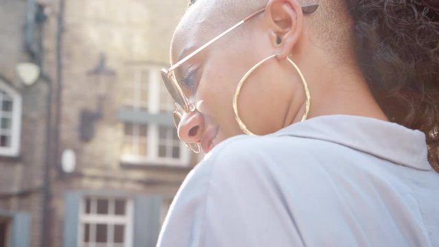 Fashionable young black woman wearing sunglasses talking on the street, close up, side view, lens flare