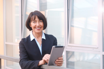 Mature businesswoman uses wireless tablet on urban street