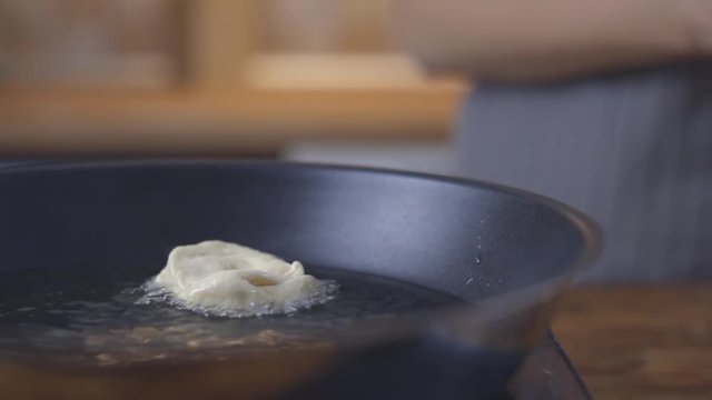 Fried doughnut. Boiling oil in a black frying pan.