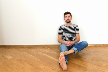 A young man is sitting on the floor in a new apartment.