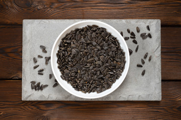 sunflower seeds in a white plate on a concrete tile on a  wooden background