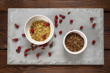 rosehip berries and medical herbs in a white bowl on a concrete slab. Dark  background