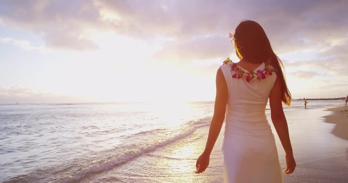 Hawaii Travel Vacation. Happy serene woman on hawaii beach enjoying sunset and freedom on hawaiian beach wearing dress and lei with arms stretched out. Girl enjoying sun in meditation zen. RED EPIC.