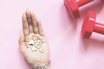 Woman's hand holding mini hearts and dumbbells on pink background. Health and Insurance