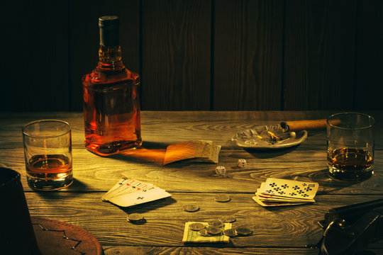 Table with playing cards, whiskey, cigar and weapons