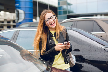 Horizontal portrait of young girl with long hair in glasses walking on parking zone. She wears...