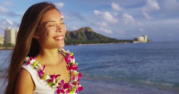 Hawaii travel beach vacation - woman smiling happy wearing traditional Hawaiian flower Lei. Pretty mixed race Asian Caucasian woman on beach resort., Waikiki, Oahu, Hawaii, USA. RED EPIC SLOW MOTION.