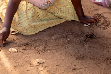 Extreme close up of a young girl wirting and drawing in the sand as she has no access to western...