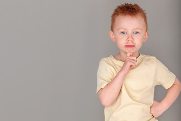 Fiery redhead young boy in yellow shirt in finger to chin in deep thought stance in landscape...