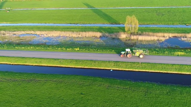 Aerial view of tractor carrying farm implement driving fast over public road moving backwards and upwards showing more of the rural agricultural surroundings 4k high resolution quality footage
