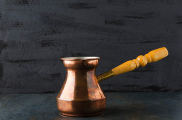 Closeup  of rustic cezve on black table against dark wall,copy space