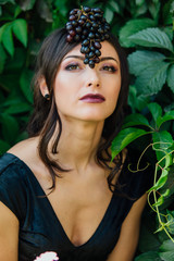 Portrait of young sexy brunette with black grapes on head.