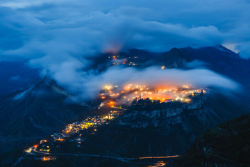 Gunib highland village on a mountain plateau in the clouds with colorful lights at night. Popular tourist place. Beautiful landscape with long exposure. Caucasus Mountains, Dagestan Republic, Russia