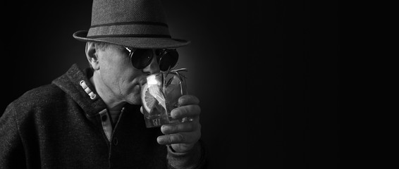 Middle-aged man in a hat drinking an alcoholic cocktail with lemon.