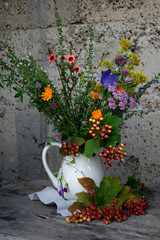 Bouquet of summer flowers in a white jug against the background of the old wall