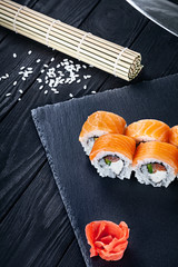 Close up view on sushi rolls with with red fish, okra and Philadelphia cheese on a black coal board and a wooden background. Traditional Japanese cuisine. Food with copy free space for text, logo.