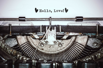 Old vintage typewriter, retro machine with white sheet of paper and typed text "Hello, Love!", copy space, close up