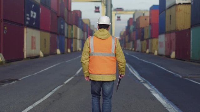 Engenier in white helmet and uniform walking through shipping dock for checking.