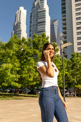 Portrait of a beautiful smiling young woman in a white shirt while talking on her phone on a sunny day.