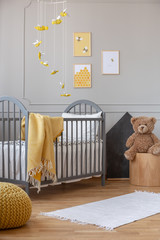 Yellow blanket on grey wooden crib in fashionable baby room with posters on the wall