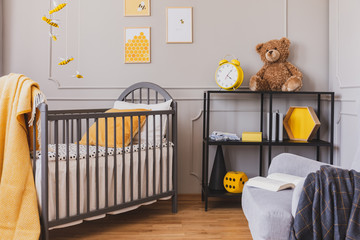 Black metal industrial shelf with teddy bear and yellow clock next to wooden crib with white...