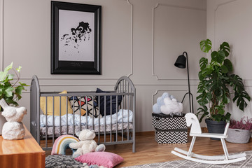 Poster above cradle next to toys in grey kid's bedroom interior with plant and rocking horse. Real photo
