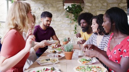 A multi-ethnic group of mixed age adult friends eating lunch together at table in a restaurant raise their glasses in a toast, side view