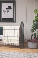 Pouf and plant next to bed with blanket in grey baby's bedroom interior with poster. Real photo