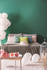 Birthday party in bedroom with large bed with pillows and moss green blanket, copy space on the empty green wall