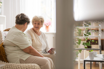 Two senior woman sitting on couch learning together how to use a mobile phone