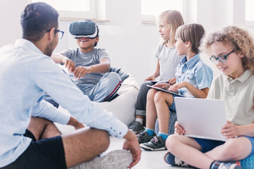 Happy boy uses VR glasses during technology lesson for kids at school